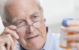 Male senior with glasses looking at a pill bottle