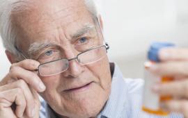 Male senior with glasses looking at a pill bottle